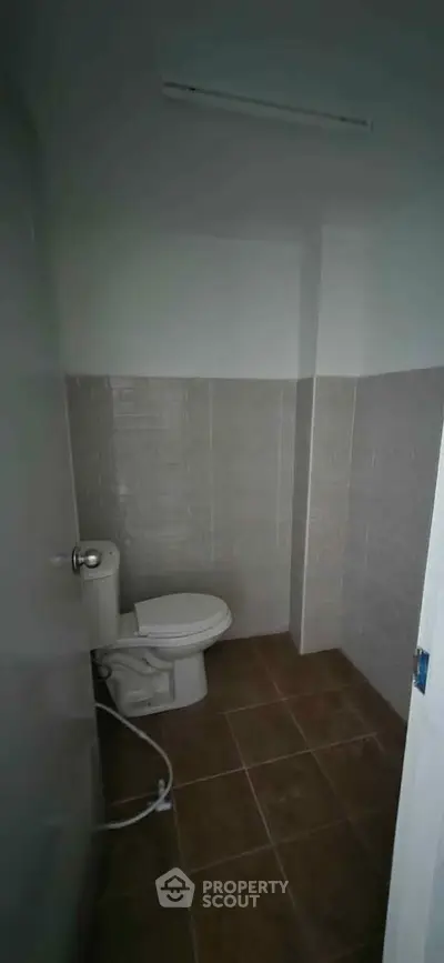 Compact bathroom with tiled walls and floor, featuring a standard toilet.