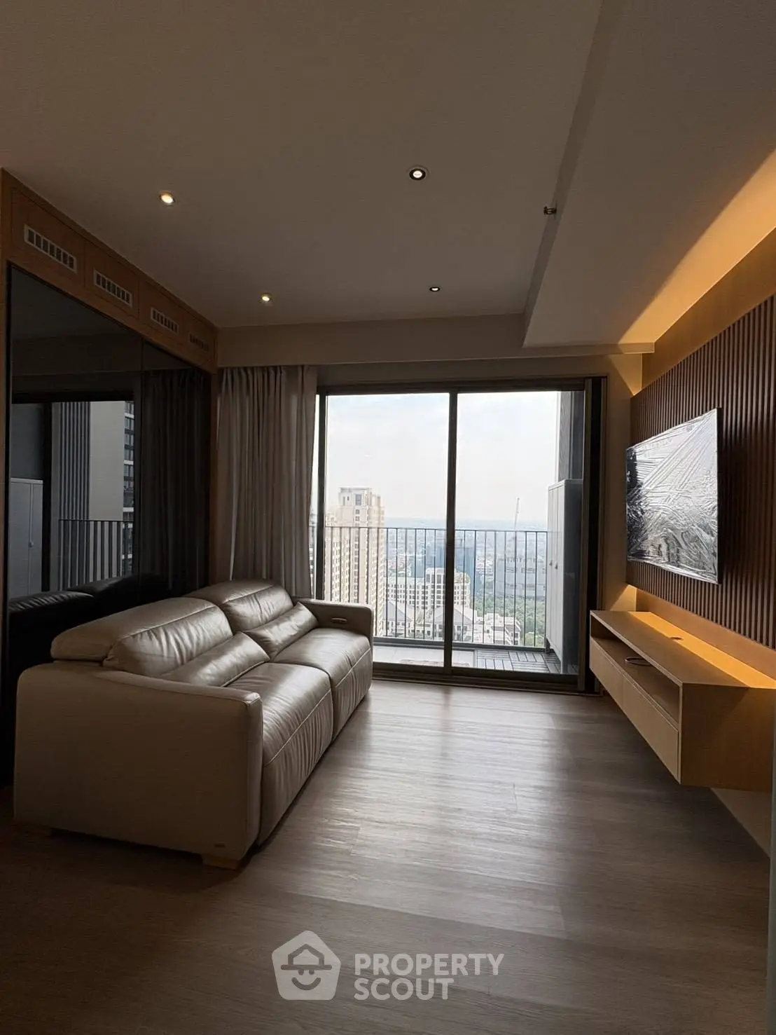 Modern living room with large windows and balcony offering stunning city views.