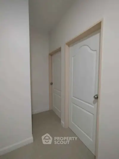 Minimalist hallway with two white doors and neutral tile flooring
