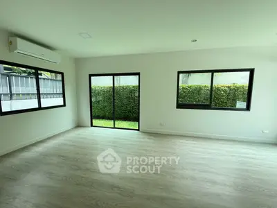 Spacious modern living room with large windows and garden view, featuring sleek flooring and air conditioning.
