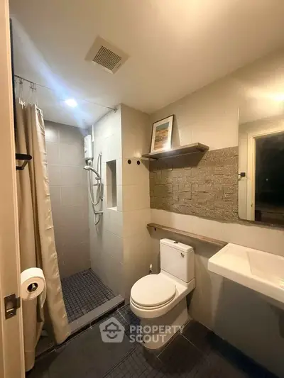 Modern bathroom with shower, toilet, and sleek sink in a cozy real estate unit.