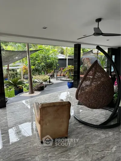 Luxurious indoor-outdoor living space with modern swing chair and lush garden view.