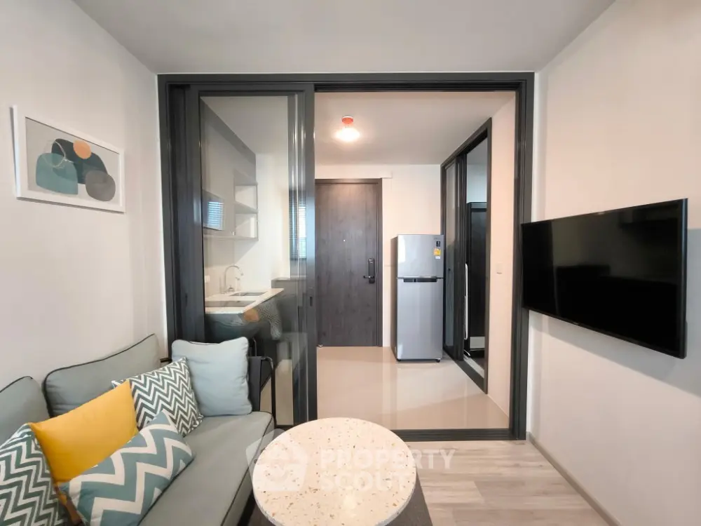 Modern living room with sleek design, featuring a cozy sofa, wall-mounted TV, and a glimpse of a compact kitchen.