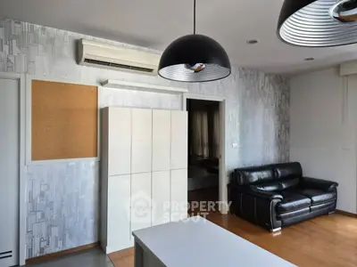 Modern living room with stylish lighting and black leather sofa, featuring a minimalist design and air conditioning.