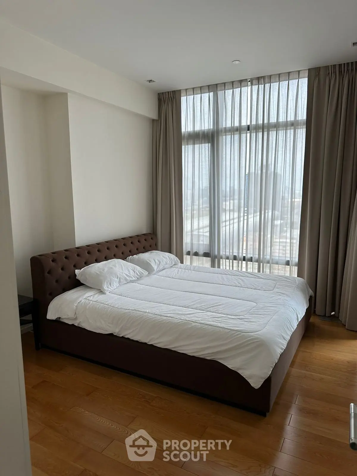 Spacious bedroom with large windows and elegant curtains, featuring a comfortable double bed.