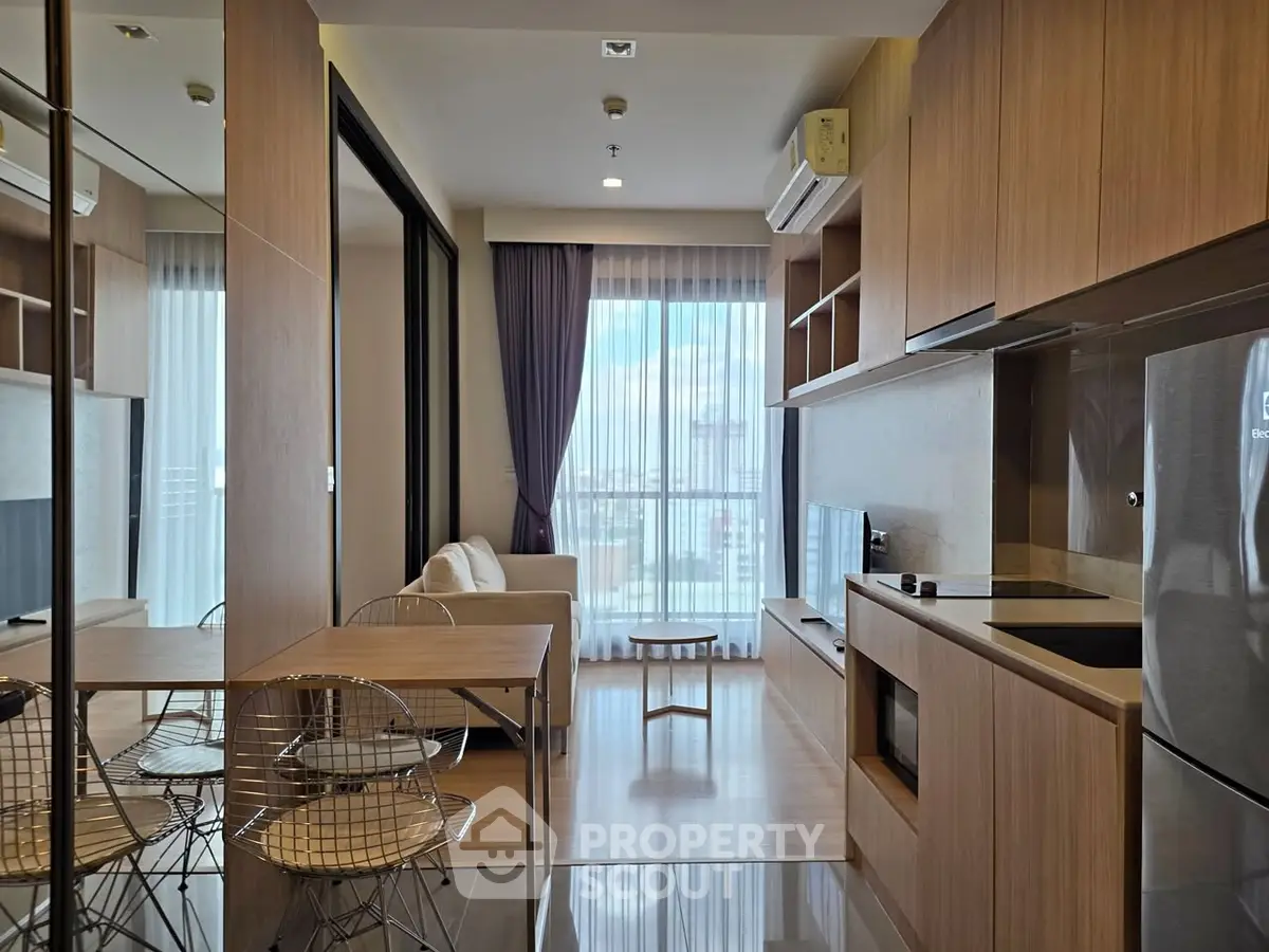 Modern open-layout living room with kitchen, featuring sleek wooden cabinetry and large windows.