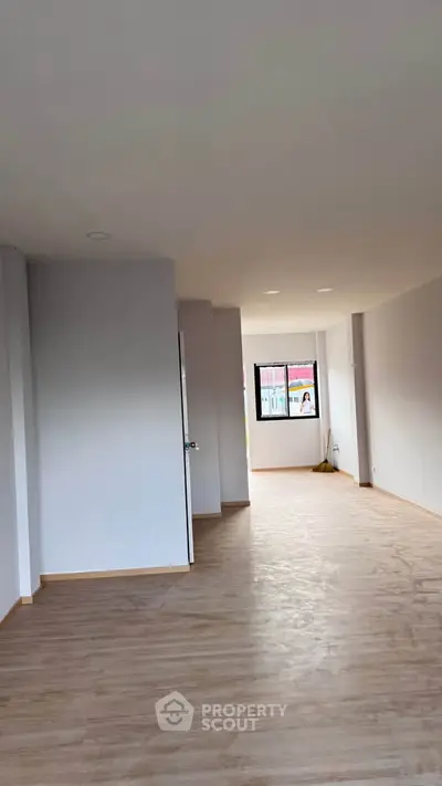 Spacious empty room with wooden flooring and large window, ideal for customization.