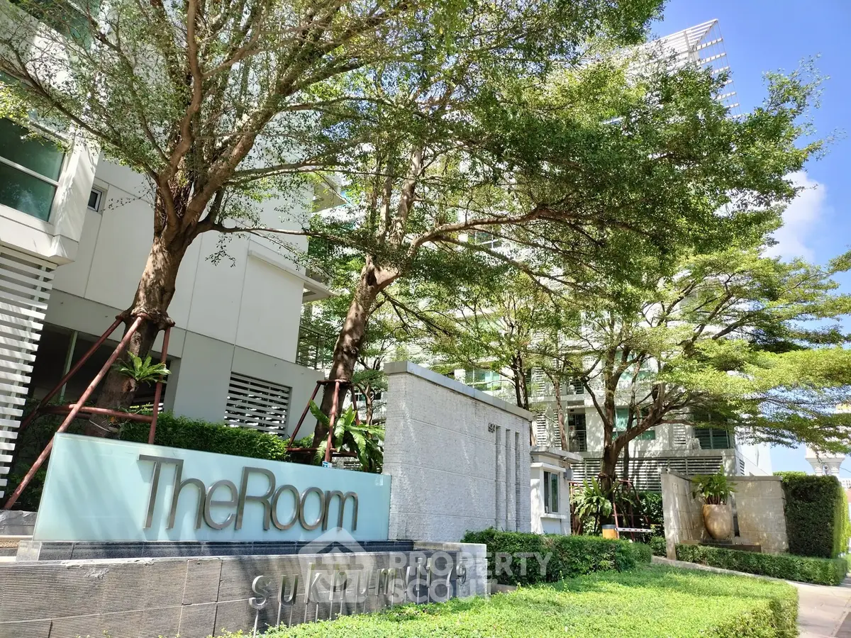 Modern condominium entrance with lush greenery and stylish signage in urban setting.