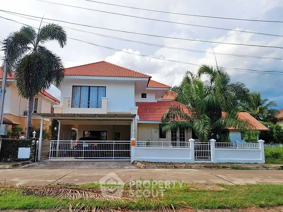 Charming two-story house with red-tiled roof and lush palm trees in a serene neighborhood.