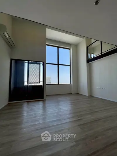 Spacious modern living room with high ceilings and large windows offering natural light and city views.