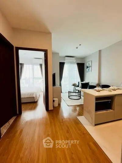 Modern open-plan living room with kitchen and bedroom view, featuring sleek wooden flooring.