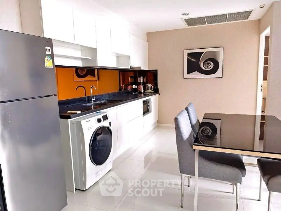 Modern kitchen with sleek appliances and dining area, featuring a washing machine and stylish decor.