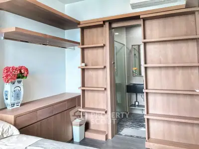 Modern bedroom with built-in wooden shelves and ensuite bathroom, featuring elegant decor and natural light.