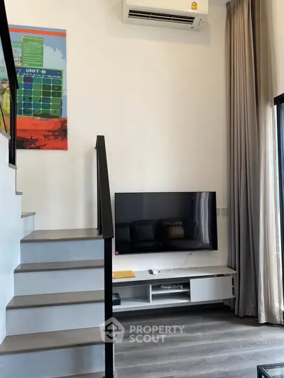 Modern living room with sleek staircase and wall-mounted TV, featuring stylish decor and natural light.