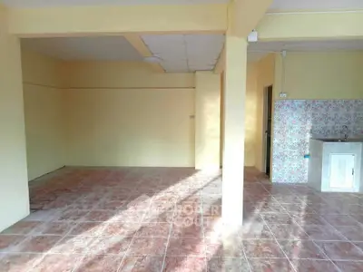 Spacious open-plan room with tiled flooring and partial kitchen area, ideal for customization.