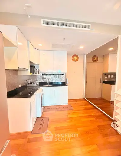 Modern kitchen with sleek white cabinets, black countertops, and hardwood floors in a stylish apartment.