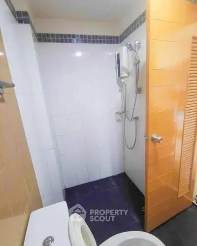 Compact bathroom with shower and toilet, featuring modern tiles and wooden door.