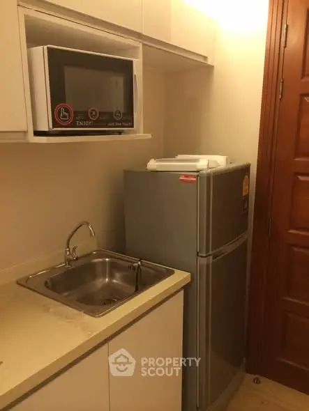 Compact kitchen with microwave, fridge, and sink in modern apartment.