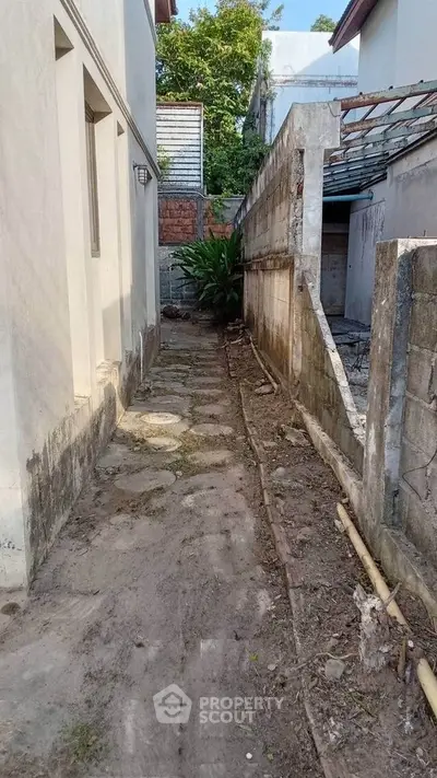 Narrow side alley between residential buildings with concrete path and greenery