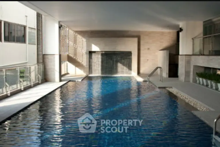 Luxurious indoor pool with modern design and waterfall feature in upscale property