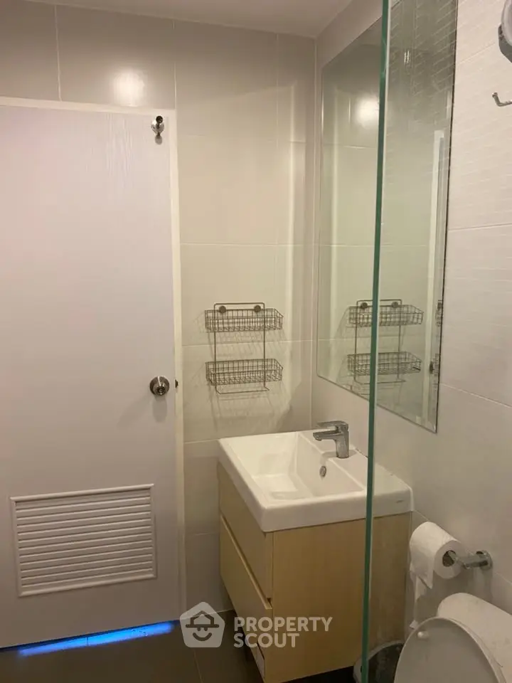 Modern bathroom with sleek fixtures and neutral tiles, featuring a compact vanity and glass shower partition.