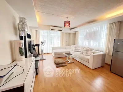 Spacious living room with modern decor and natural light, featuring a cozy white sofa and wooden flooring.