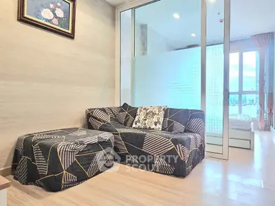 Modern living room with stylish sofa and glass partition leading to a bright bedroom.