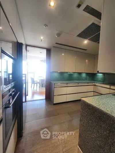 Modern kitchen with sleek cabinetry and open layout leading to dining area.