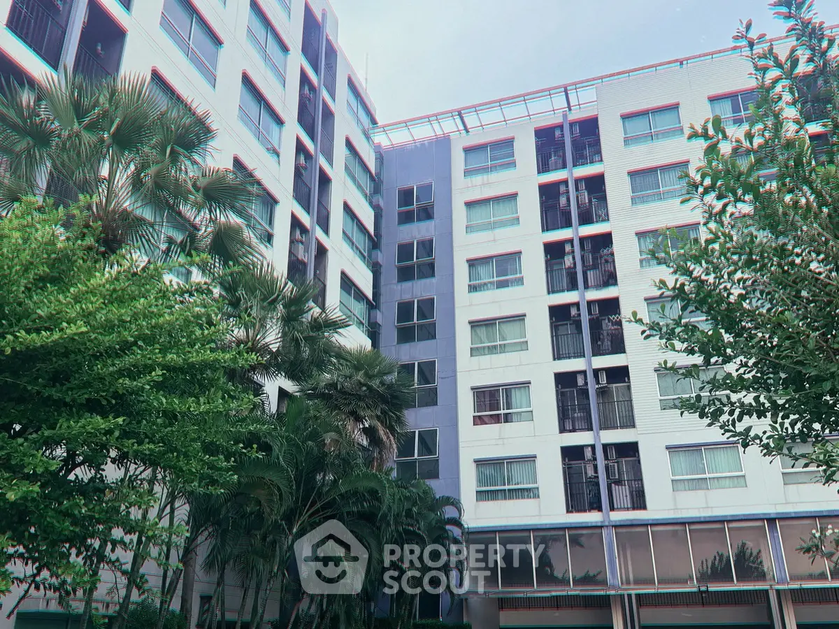 Modern apartment building exterior with lush greenery and tall windows.