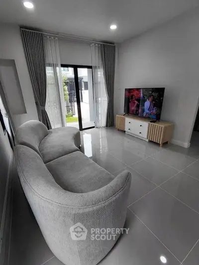 Modern living room with sleek gray sofa and large TV, featuring elegant floor-to-ceiling curtains and glossy tile flooring.
