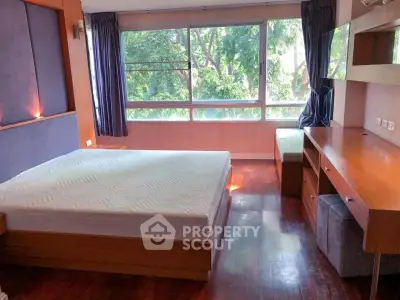 Spacious bedroom with large windows and wooden furniture in a serene setting.