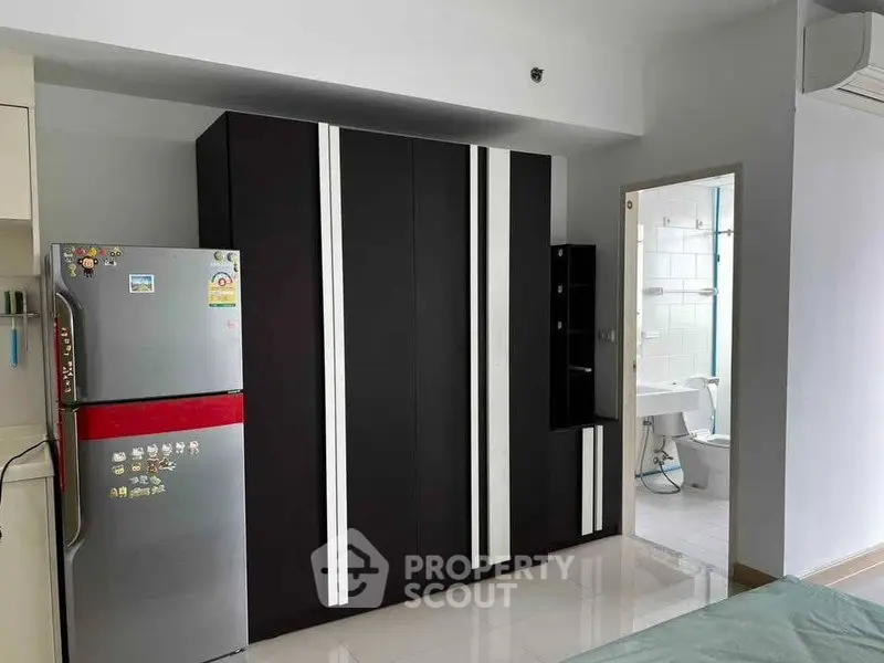 Modern apartment interior with sleek wardrobe and stainless steel fridge near bathroom entrance.
