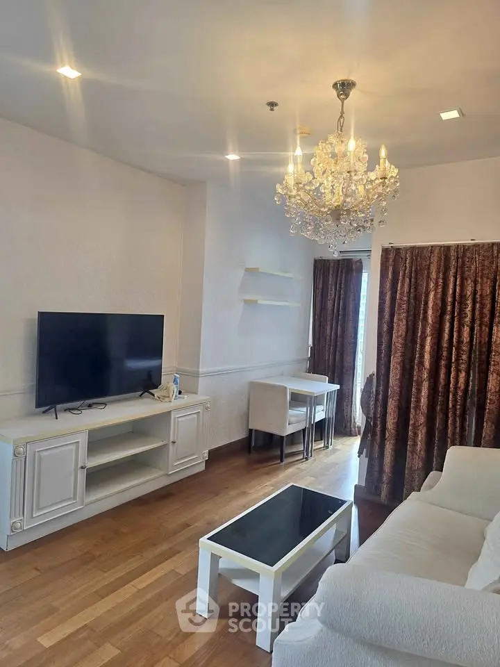 Elegant living room with chandelier, TV, and stylish furniture in a cozy apartment.