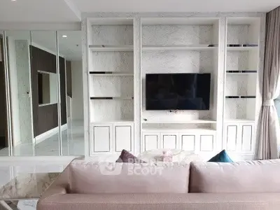 Modern living room with built-in shelves and flat-screen TV, elegant sofa, and stylish decor.