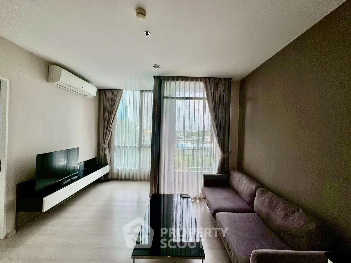 Modern living room with large windows and sleek furniture in a high-rise apartment.