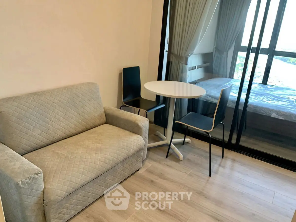 Cozy living area with sofa and dining set, adjacent to a bedroom with large windows.