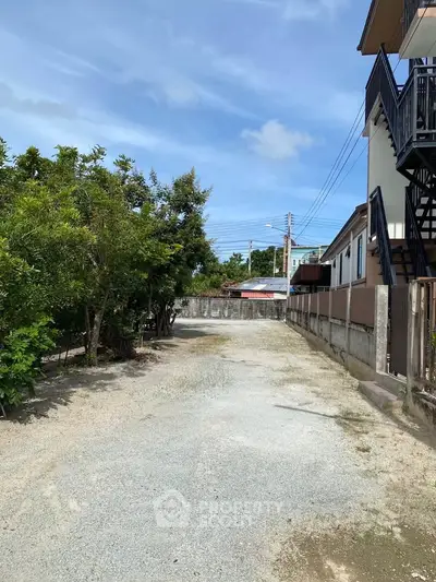 Spacious gravel driveway leading to residential property with lush greenery and clear blue sky.