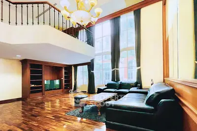 Luxurious living room with high ceilings, elegant chandelier, and large windows offering natural light.