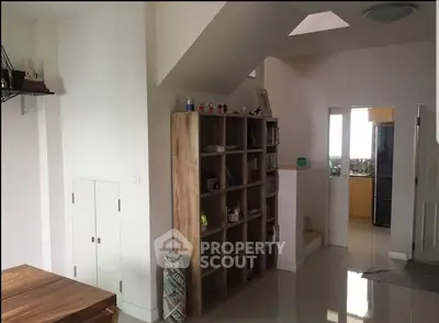 Modern living area with open shelving and kitchen view, featuring sleek design and natural light.