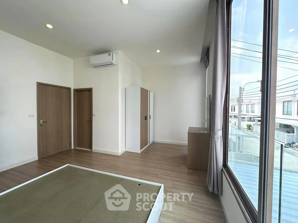 Spacious modern bedroom with large window and wooden flooring in a contemporary home.