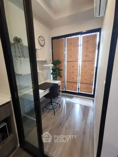 Modern study room with glass door, wooden flooring, and natural light from large windows.