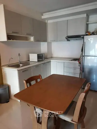 Modern kitchen with sleek cabinetry, dining table, and stainless steel appliances in a cozy apartment.