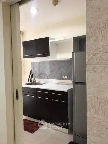 Modern kitchen with sleek cabinets and stainless steel fridge in compact layout.