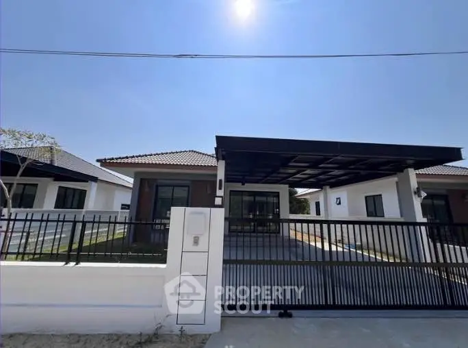 Modern single-story house with spacious driveway and sleek gate under clear blue sky.