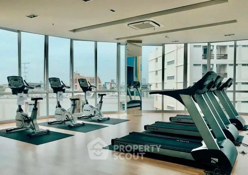 Modern gym with treadmills and exercise bikes in a high-rise building with city views.