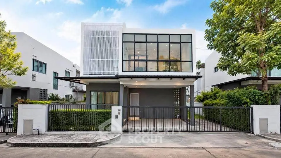 Modern two-story house with large windows and gated entrance in a serene neighborhood.