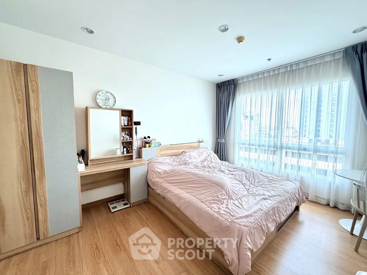Spacious bedroom with natural light and modern furnishings in a high-rise apartment.