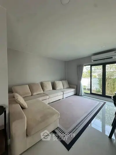 Spacious living room with modern sofa and large window offering natural light and garden view.