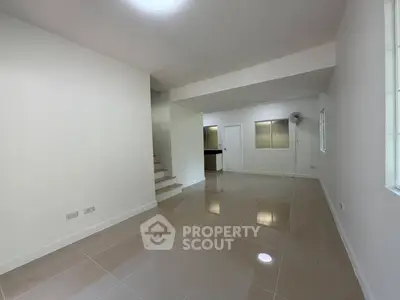Spacious modern living room with glossy tiled floors and neutral walls, featuring a staircase and ample natural light.