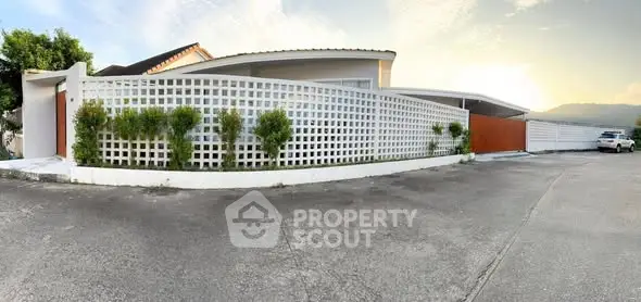 Modern house exterior with unique lattice fence and spacious driveway at sunset.